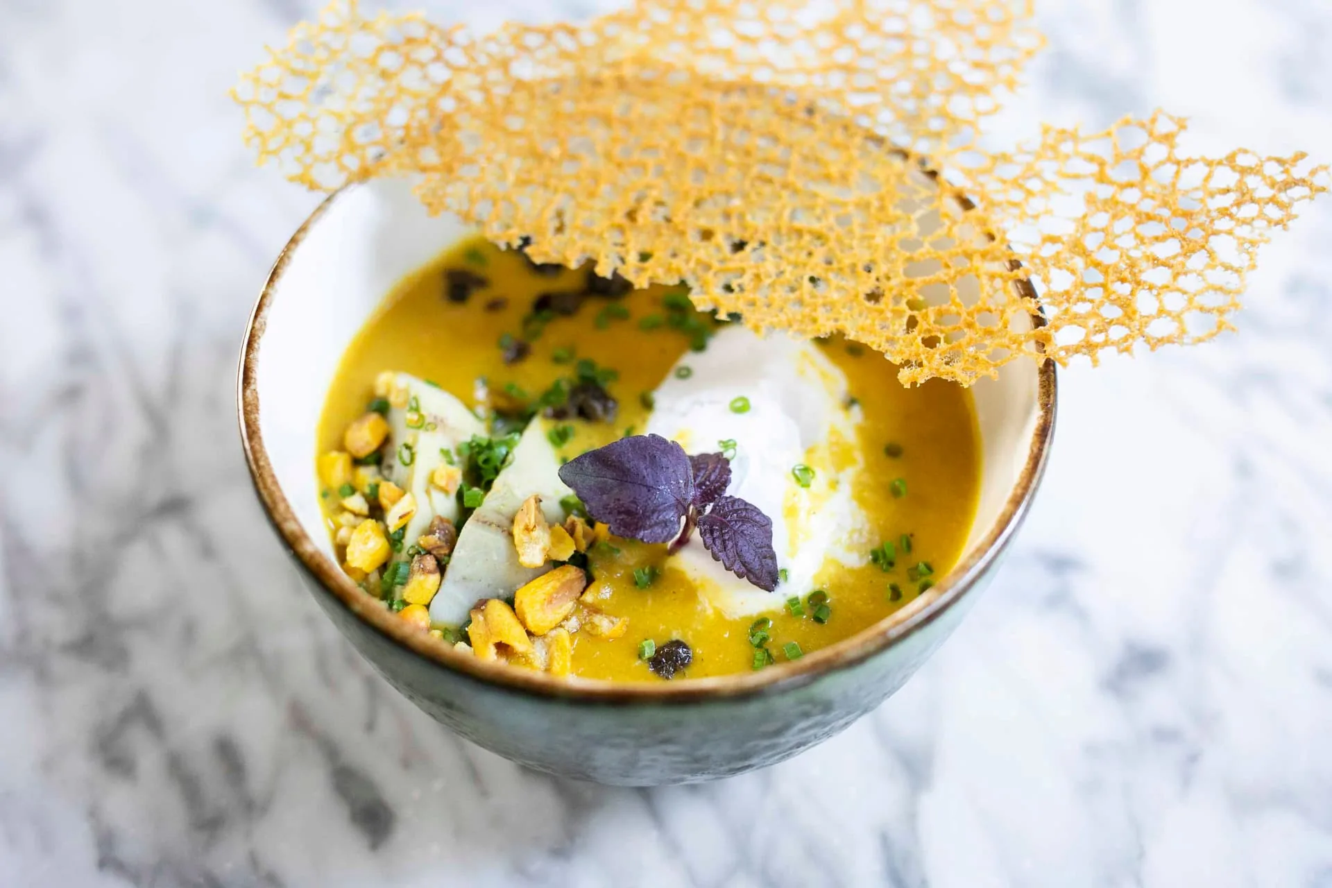 Plantaardige soep met een crunchy garnering en paars blad, geserveerd bij WAKU WAKU