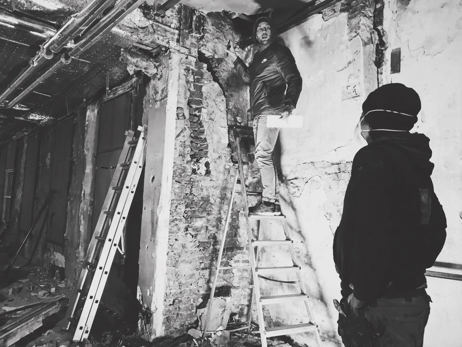 Zwart-witbeeld van bouwinspectie op een ladder bij de bakstenen muur van het pand
