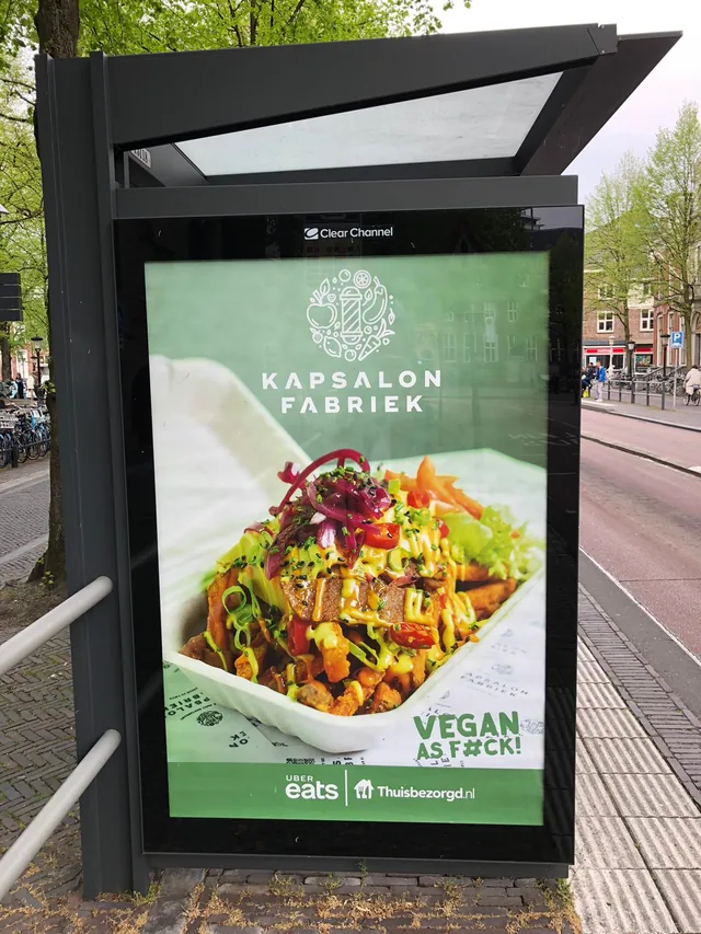 Abri-reclame voor Kapsalonfabriek met een plantaardige kapsalon in beeld