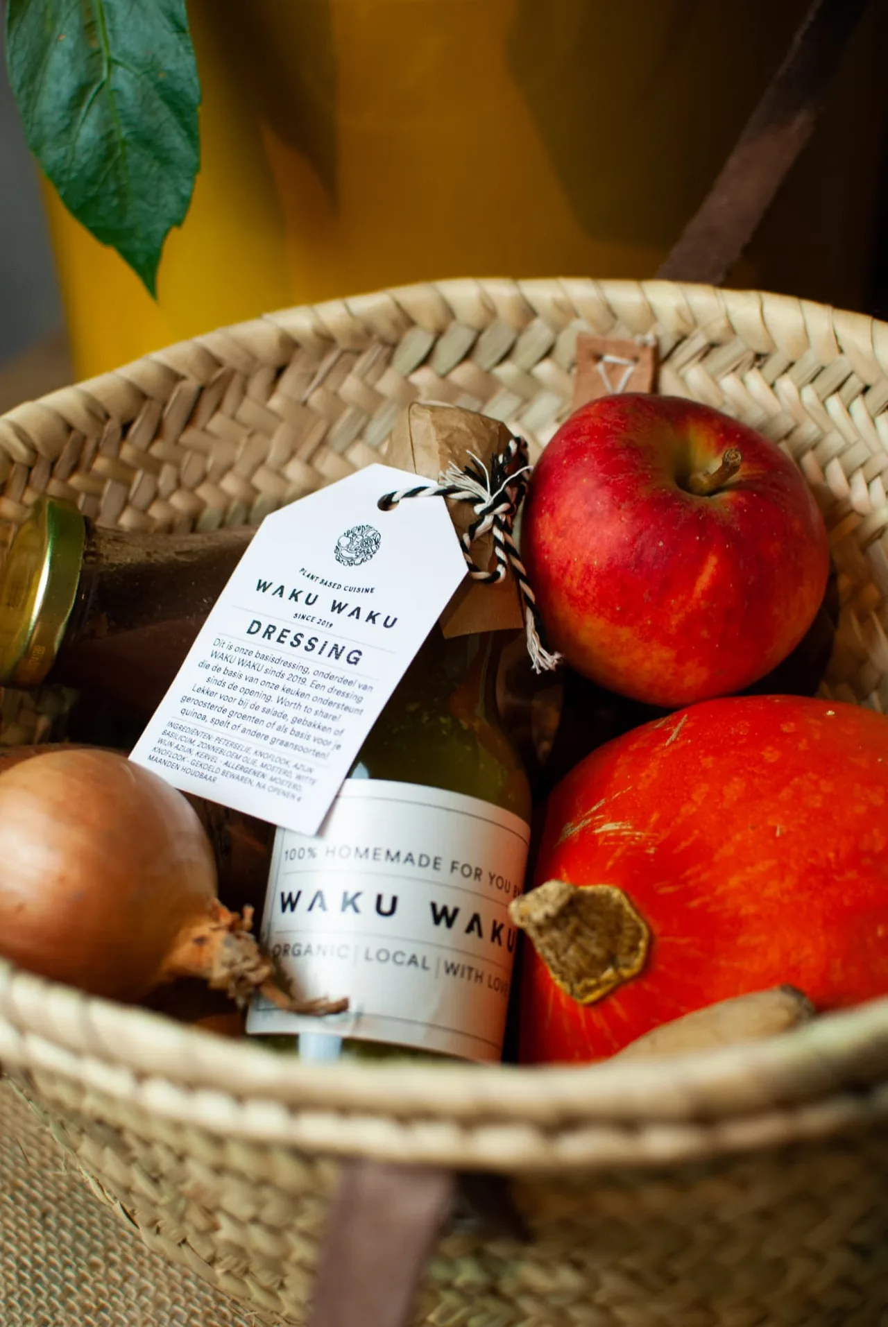 Fles WAKU WAKU-dressing in een mand met appels en een pompoen